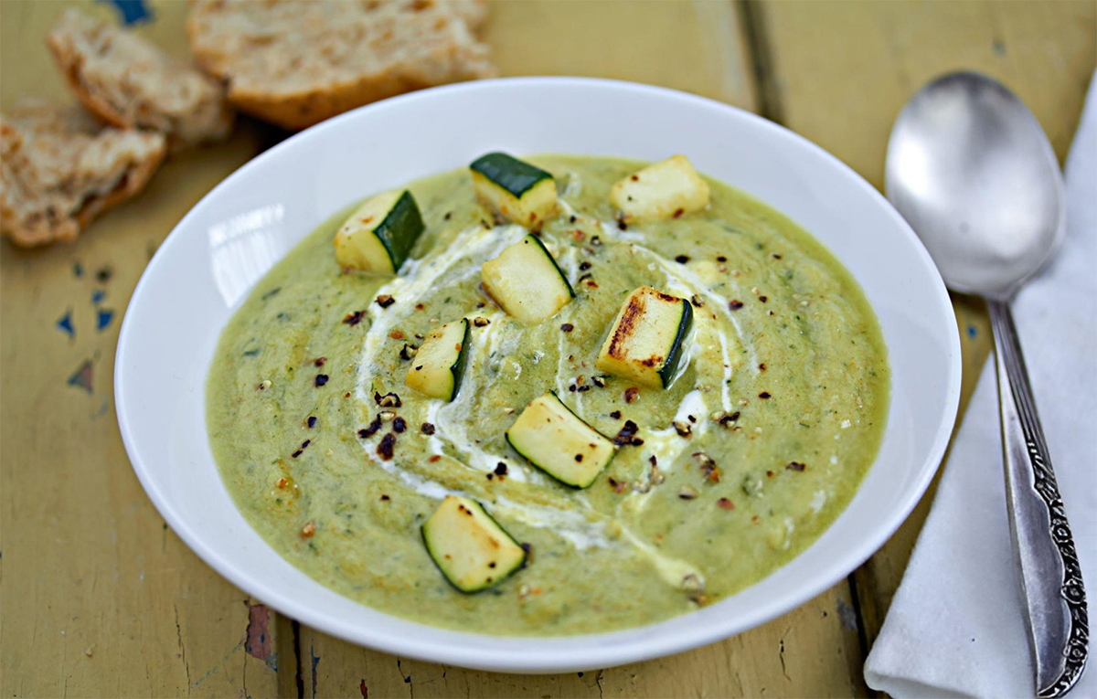 healthy zucchini soup in a white bowl with chunks of zucchini