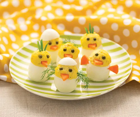 deviled eggs as little chicks on a green and white striped plate