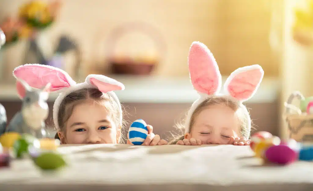 two children with bunny headbands peeking over a table