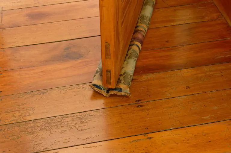 A double draft stopper made from fabric slides under a wooden door and moves with the door when it is opened