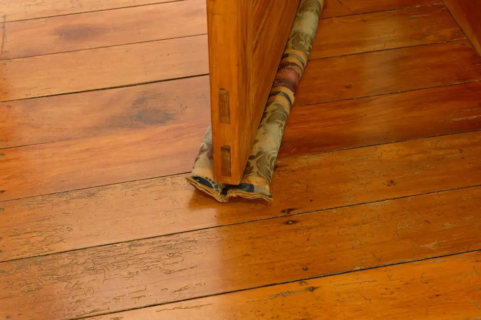 A DIY Under Door Draft Stopper made from fabric slides under a wooden door and moves with the door when it is opened
