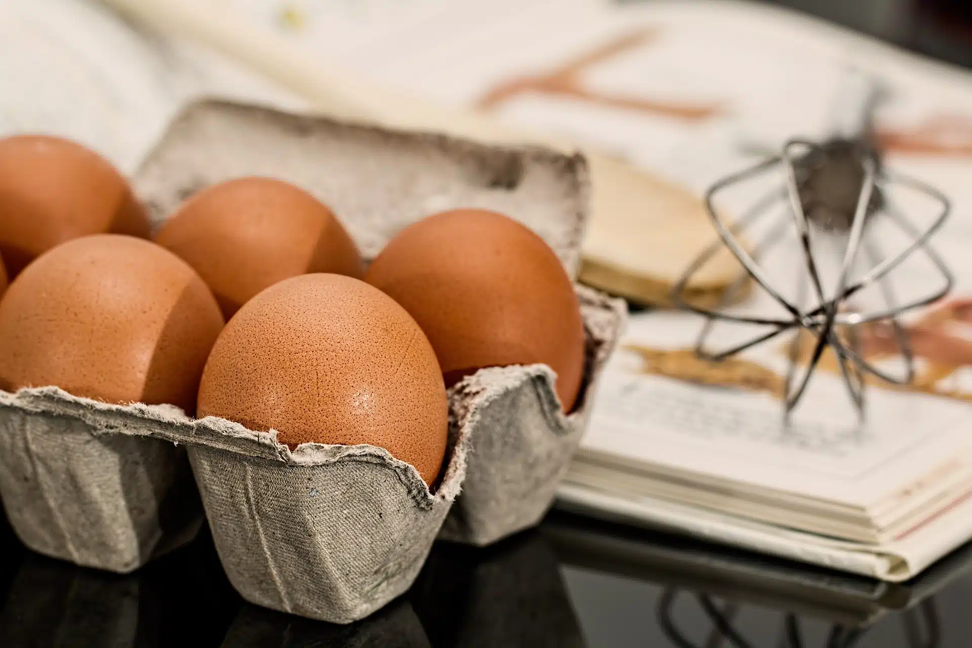 eggs in carton beside wire whisk