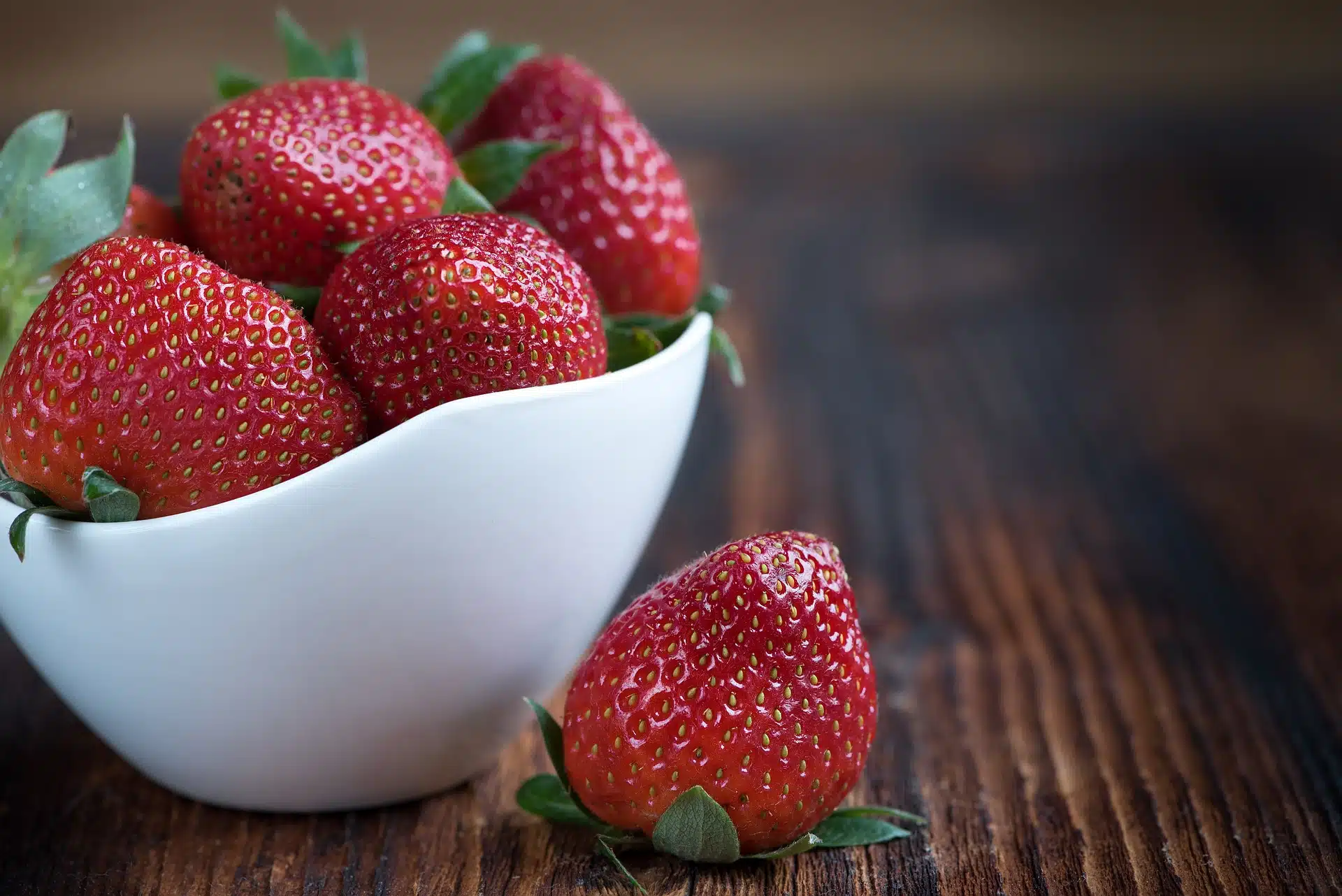 strawberries in white bowl on wood table