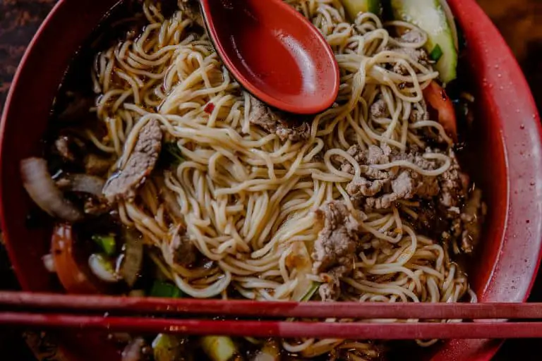 red spoon on top of noodles with pepper steak