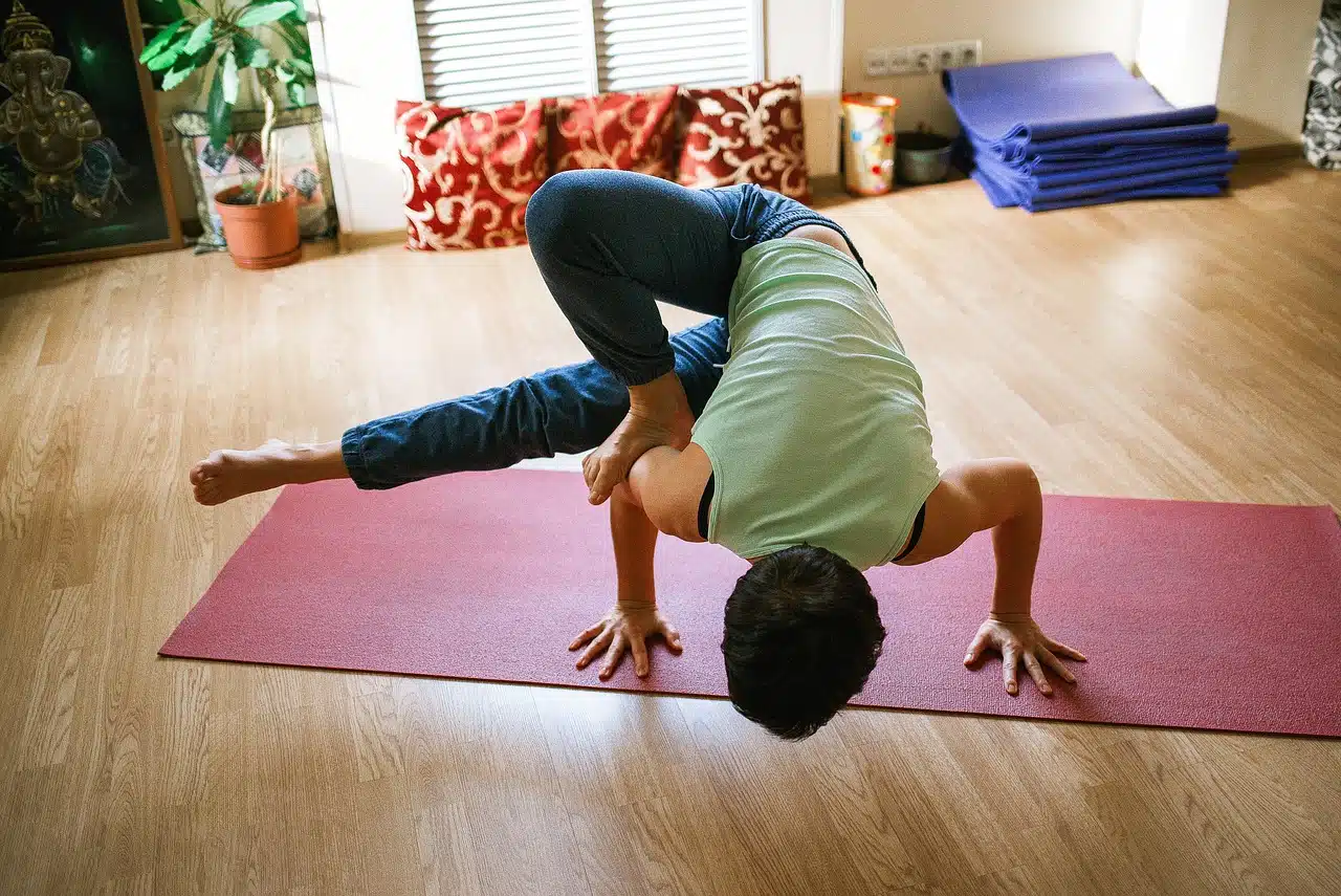 person with light green shirt on maroon yoga mat in yoga pose