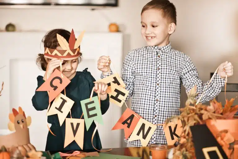 Kid holding paper garland with text Give thanks. Children decorating living room for celebrating Thanksgiving day