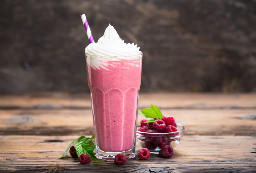 pink milkshake with whipped cream, striped straw and raspberries on wooden table