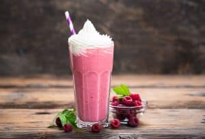 pink milkshake with whipped cream, striped straw and raspberries on wooden table