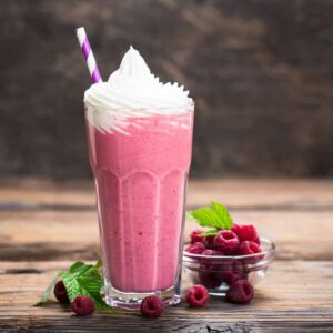 pink milkshake with whipped cream, striped straw and raspberries on wooden table