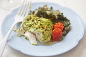 pesto baked cod with cherry tomatoes and greens on white plate