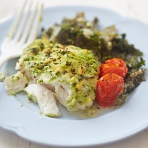 pesto baked cod with cherry tomatoes and greens on white plate