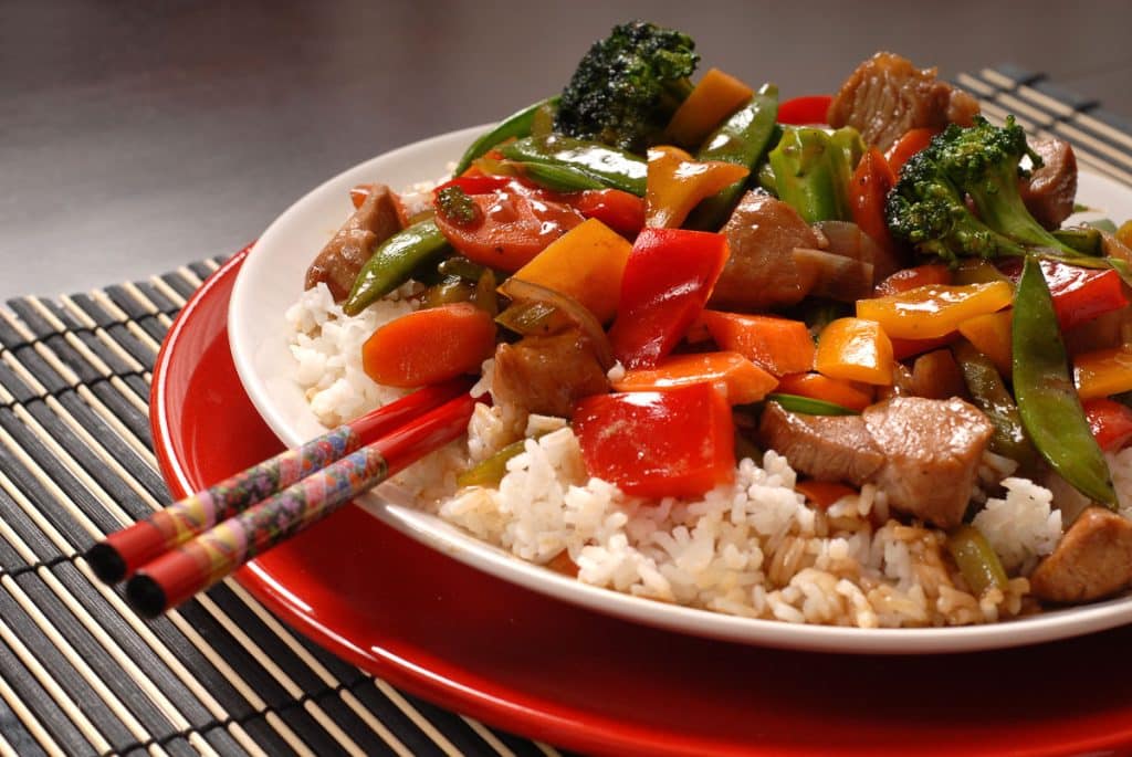 pork stir fry with vegetables served on rice on red plate