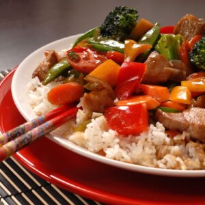 pork stir fry with vegetables served on rice on red plate