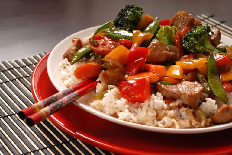 pork stir fry with vegetables served on rice on red plate