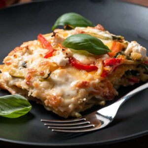 fork on black plate with vegetable lasagna and 3 basil leaves