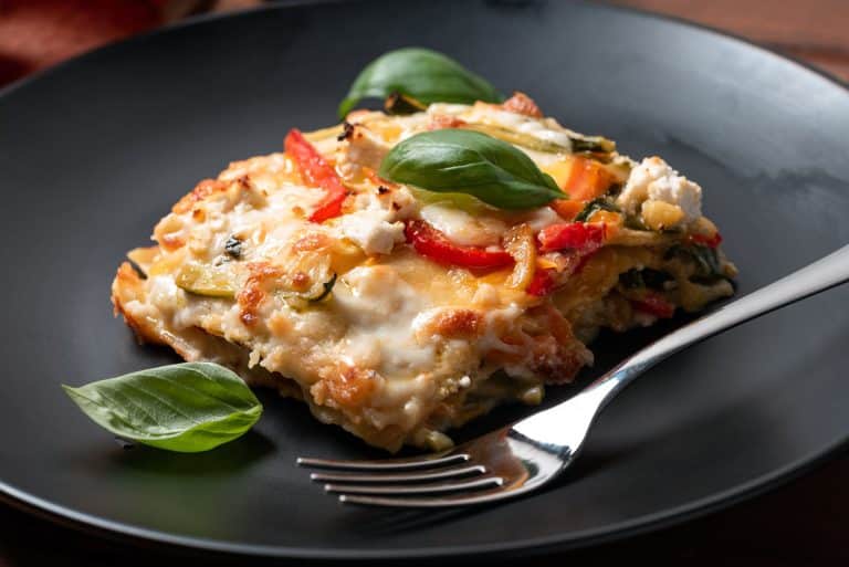 fork on black plate with vegetable lasagna and 3 basil leaves