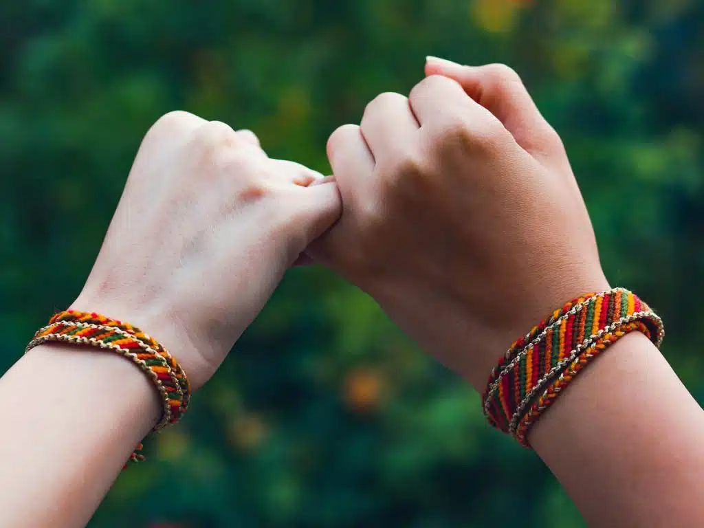 two hands grabbing pinky fingers with friendship bracelets on wrists