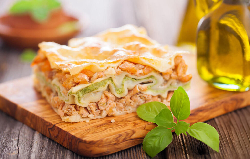 piece of seafood lasagna with herb sprig on wooden tray