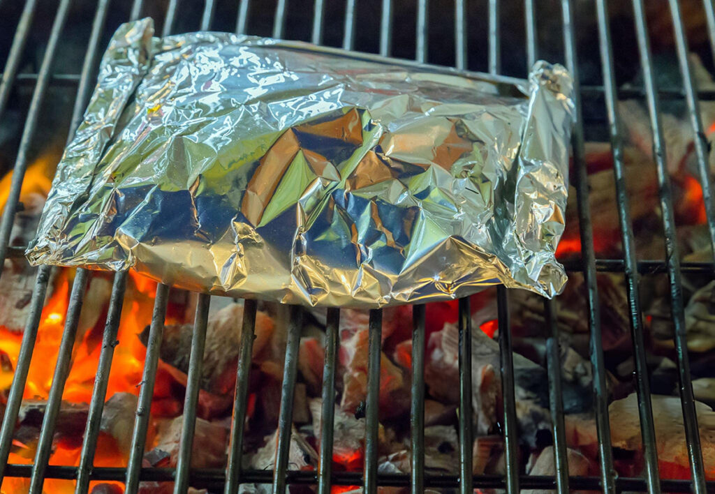 burritos wrapped in aluminum foil on charcoal grill
