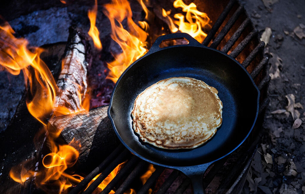 pancakes in black cast iron pan over open fire