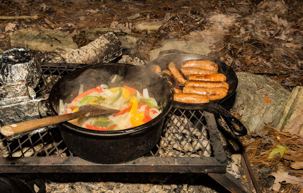 sausage with peppers and onions cooking on charcoal grill