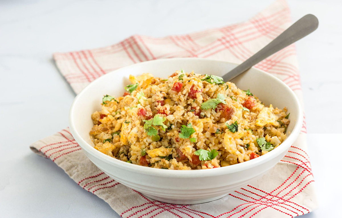 Cauliflower fried rice in a white bowl with silver spoon